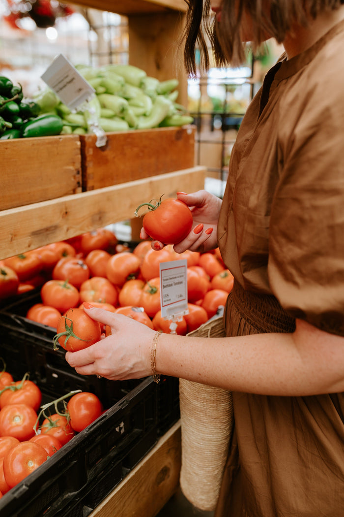 woman in a farmer's market picking up a tomato